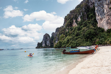 Naklejka na ściany i meble Tourist canoeing with wooden boat and mountain on coastline in tropical sea at Phi Phi Island