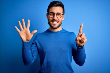Young handsome man with beard wearing casual sweater and glasses over blue background showing and...