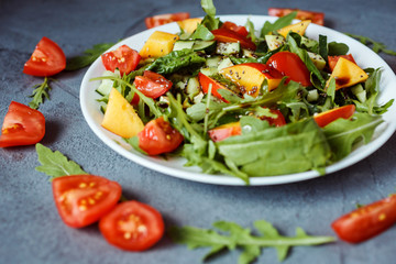 Close up photo of tasty colorful salad made of ruccola, cherry tomatoes, spinach, nectarine, chia seeds. Gray background is decorated with aragua and tomatoes.