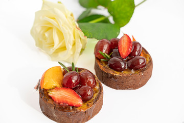 Two tasty chocolate cakes with icing fruits and berries on white background with white rose,...