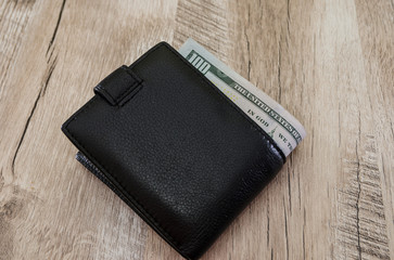 dollars in a black wallet on a wooden background. View from above.