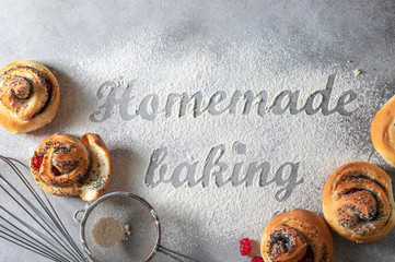 The inscription on the flour Homemade baking. Homemade buns with poppy seeds, tools and baking products on a light background.