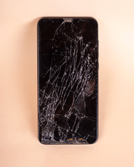 broken touchscreen black phone, smartphone, broken glass display smartphone on a beige background
