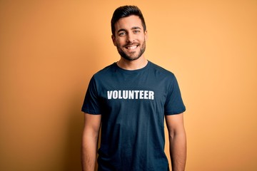 Young handsome man with beard volunteering wearing t-shirt with volunteer message with a happy face...