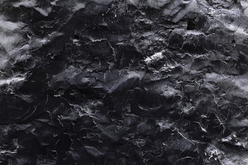 A black stone surface with an uneven texture in the form of bulges and cracks in monochrome black tones. Concept background, texture, minimalist black.