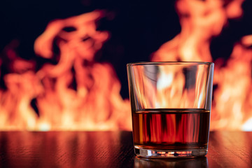 whiskey in a glass on a brown wood table with a fire in the background