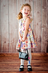 Little beautiful cheerful girl with a small black handbag in her hands. Shot in a photo studio on a wooden background.