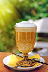 Fresh morning latte in a glass with foam on a blurry green background. Selective focus