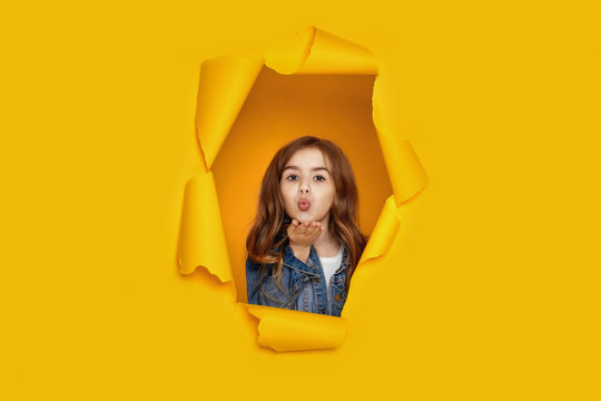 Portrait of cute happy smiling caucasian little cild girl sending kiss in yellow paper hole.