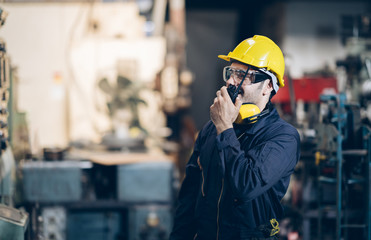 Engineer working in factory talking on walkie talkie for control machine