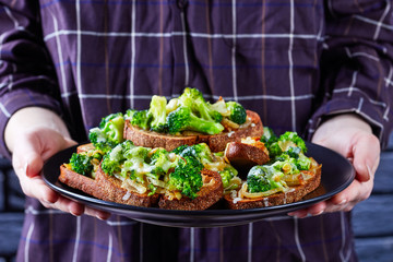 Woman holding a plate of broccoli melt sandwiches