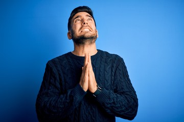Young handsome man wearing casual sweater standing over isolated blue background begging and...