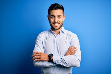 Young handsome man wearing elegant shirt standing over isolated blue background happy face smiling...
