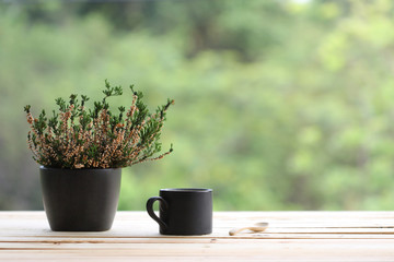 black coffee mug with heathers plant in black pot on wooden table at outdoor