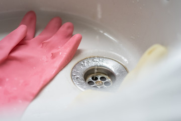 Cleaning gloves and a little water. Cleaning pink and yellow gloves and drops of water going down the drain.