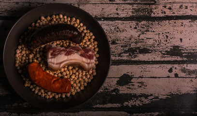 Chickpeas in a bowl prepared for cooking, accompanied by chorizo, blood sausage and bacon. Aerial view. Horizontal format.