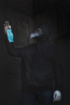 Modern stylized plague doctor in leather mask and medical latex gloves holds disposable face mask. Epidemia protection concept