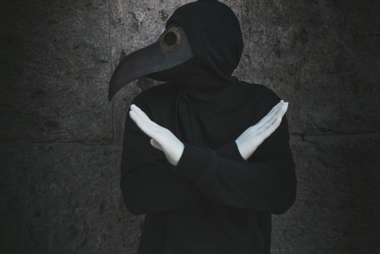 Plague doctor shows a stop sign by crossed hands. Hands in rubber medical gloves. Quarantine concept.