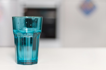 close up of a blue glass of water against the kitchen background and a vase of flowers on a white...