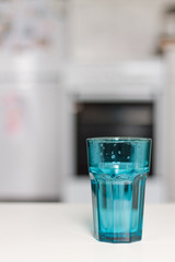 close up of a blue glass of water against the kitchen background and a vase of flowers on a white table