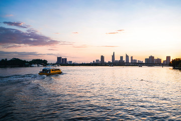 Fototapeta premium River city view landscape at twilight sunset. Boat on river with tranquil water. Hochiminh city Saigon vietnam cityscape building with Bitexco tower