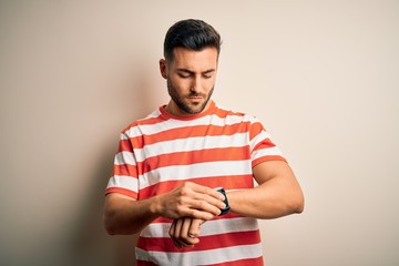 Young handsome man wearing casual striped t-shirt standing over isolated white background Checking the time on wrist watch, relaxed and confident