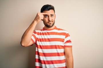 Fototapeta premium Young handsome man wearing casual striped t-shirt standing over isolated white background pointing unhappy to pimple on forehead, ugly infection of blackhead. Acne and skin problem