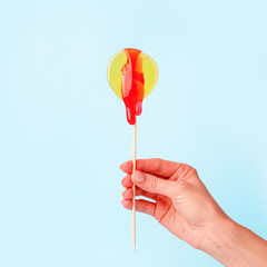 Yellow circle lollypop with droping sugar paste in hand. The concept of intimate depilation - bikini zone, hair removal with hot wax, sugar paste, female beauty, problems of intimate hygiene