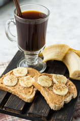 Sandwiches with peanut butter and banana and coffee for breakfast on a wooden stand