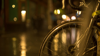 Rainy evening in the city. Shiny raindrops on a motorcycle mirror. Multi-colored city lights in the background. Creative evening lights and blurred shadows. Twilight mood. Close up.