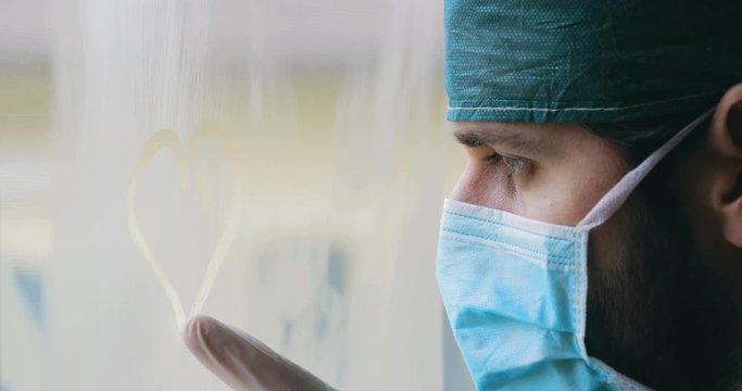 Medico disegna un cuore sul vetro appannato della finestra dell'ospedale