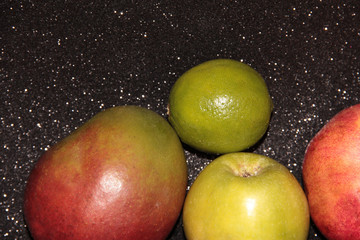 Fototapeta na wymiar Fruit on a black shiny background. Mango, pomegranate, green Apple and lime green on a black shiny background.
