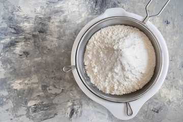 White wheat flour in a white bowl and dough sieve on a concrete background. Sift flour for yeast dough, oxygen enrichment. Top view. Copyspace for text