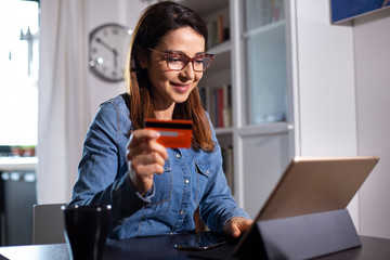 ragazza con occhiali fa un ordine con la carta di credito seduta di fronte al suo iPad a casa sua