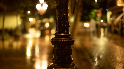 Rainy evening in the city. Shiny raindrops on a street lamp post. Multi-colored city lights in the background. Creative evening lights and blurred shadows. Twilight mood. Close up.