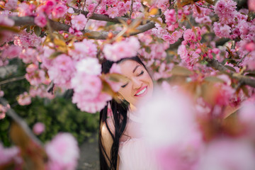Portrait of young woman in park with blooming sakura trees.
