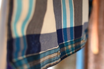 stylish light plaid shirt with gray, blue, dark blue stripes, with stylish buttons, hanging on a colored background