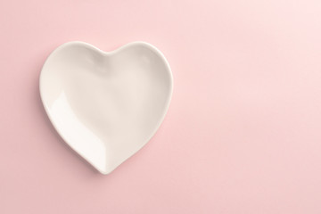 White plate in the shape of a heart on a pink delicate background. Abstract template for holiday valentines day. Close-up. Love gift concept