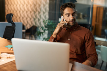 Businessman talking on a cellphone while working late