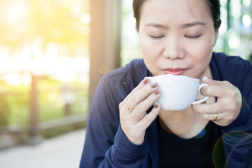 Asian girl smelling and enjoying cup of hot coffee at the outside of cafe. with sunlight effect.