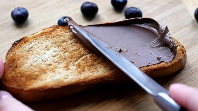 Bread with chocolate paste. Knife smear chocolate paste on a slice of bread, closeup view. Blueberries