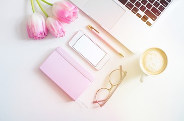 Flat lay business female workplace with mockup smartphone, keyboard laptop, coffee, and pink tulips. White colors. Minimalism. Home office. Top view. Copy space for text