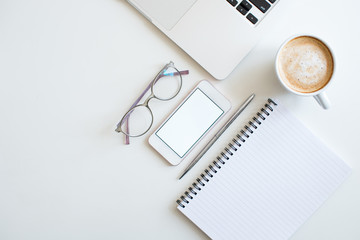 Flat lay business feminine workplace with mockup smartphone, laptop, blank notepad, coffee, glasses and green plants. White colors. Minimalism. Home office. Top view. Copy space for text