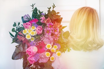 Blonde hair girl with pink spring flowers bouquet at white wall. Woman hiding head bouquet pink flowers. 