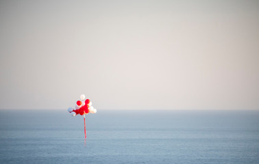 Red and white balloons fly in the sky above the sea with copy space for text. Love, happiness, valentine, wedding honeymoon concept. Happy holiday flying balloons