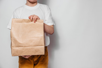 The courier guy holds in his hands a brown craft paper bag for the removal or delivery of goods and food on a white background. Place for advertising. delivery service concept