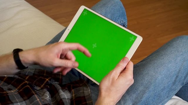 Male hands holding tablet with a green screen horizontally and swiping up
