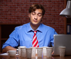 Young employee drinking coffee working at night shift