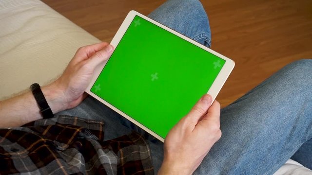 Male hands holding tablet with a green screen horizontally and watching a video