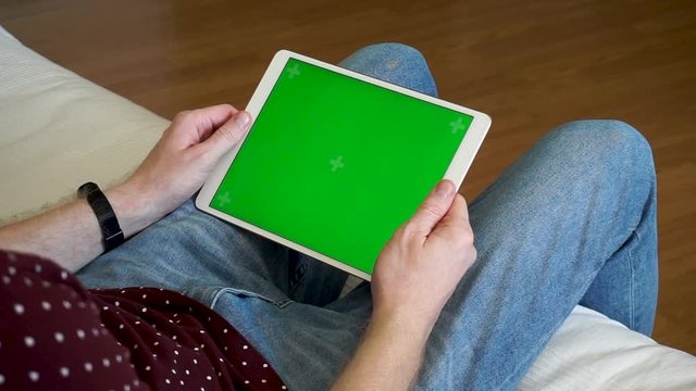 Male hands holding tablet with a green screen horizontally and watching a video